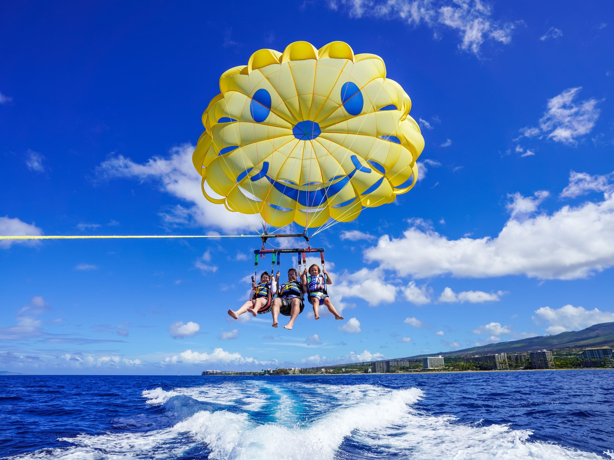 Three flyers under the yellow smiley parasail above Kāʻanapali Beach